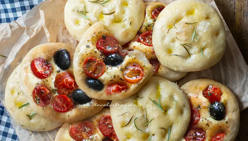 Focaccine in padella, alcune condite con pomodorini e olive, altre con rosmarino e olio. Perfette per uno spuntino.
