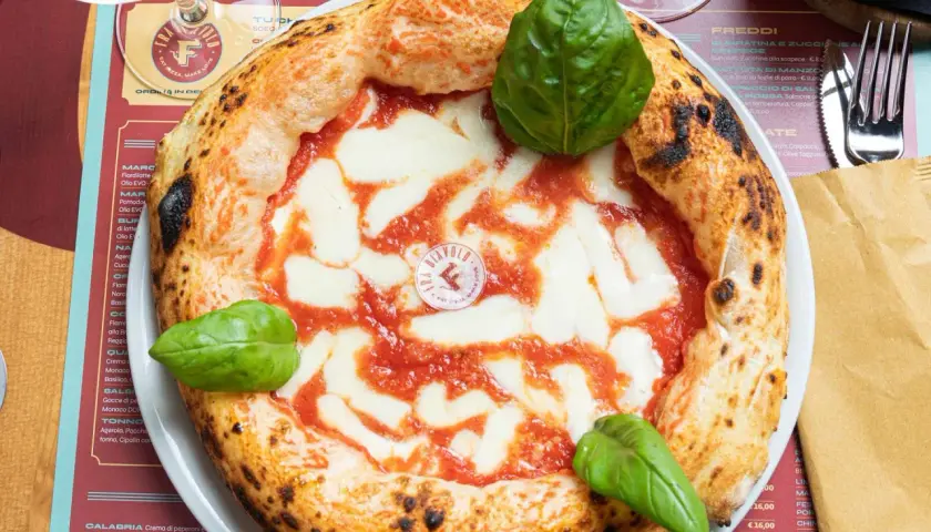Impasto pizza napoletana con pomodoro, mozzarella filante e basilico fresco. La crosta è alta e alveolata, segno di una lievitazione perfetta.