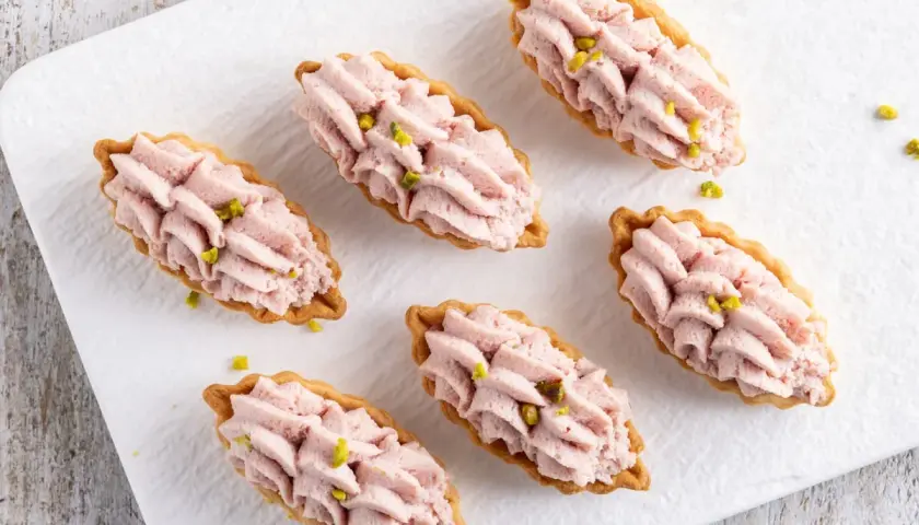 Piccoli cestini di pasta brisée ricetta, ripieni di crema rosa e guarniti con pistacchi.