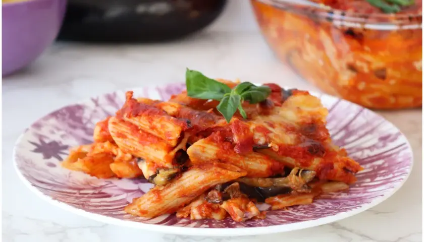 Piatto di pasta alla siciliana con melanzane, pomodoro e basilico, appena sfornata.