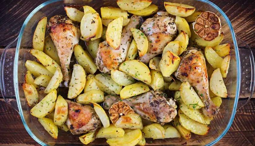 Un succulento pollo e patate al forno, dorati e profumati, in una teglia di vetro.