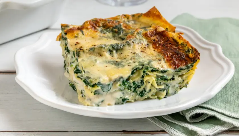 Una fetta di lasagne ricotta e spinaci, dorata al forno, su un piatto bianco.