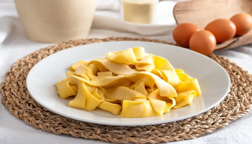 Piatto di pasta fresca fatta in casa, con uova e farina sullo sfondo.
