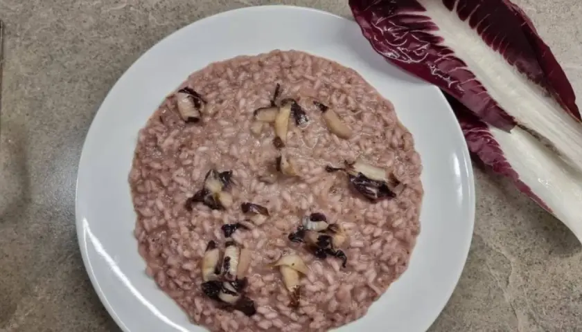 Un cremoso risotto al radicchio rosso, con pezzetti di verdura che spuntano. Accanto, una foglia di radicchio fresco.