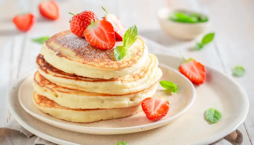 Pancake allo yogurt soffici e dorati, guarniti con fragole fresche e zucchero a velo. Un dolce inizio di giornata.