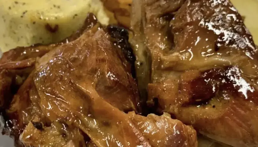 Succulento agnello al forno, dorato e lucido, servito con patate arrosto e una crema verde.