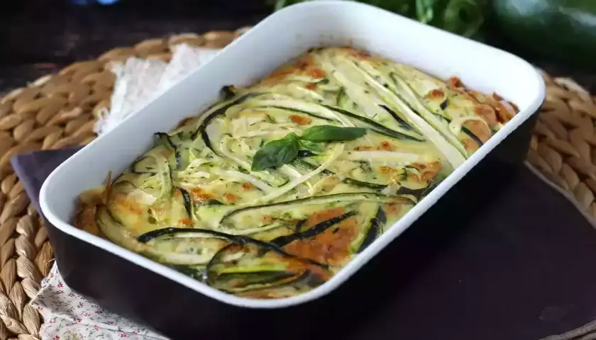 Deliziosa frittata di zucchine al forno, dorata e profumata, guarnita con basilico fresco.
