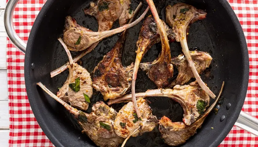 Costine di agnello in padella, dorate e succulente, pronte per essere gustate.