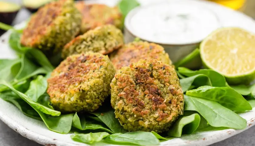 Polpette di spinaci dorate su un letto di spinaci freschi, con una ciotola di salsa e spicchi di lime.