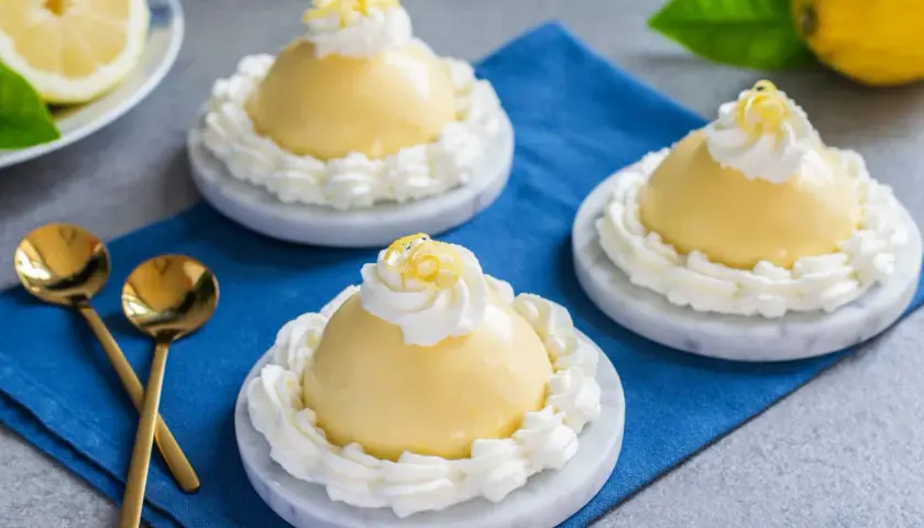 Tre deliziose delizie al limone, guarnite con panna montata e scorza di limone, su piattini di marmo.