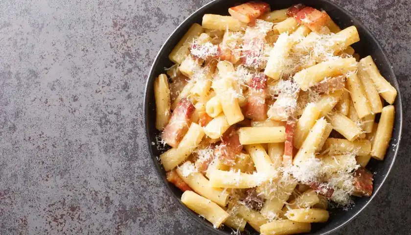 Rigatoni alla gricia fumanti, conditi con guanciale croccante e pecorino romano grattugiato, un classico della cucina romana.