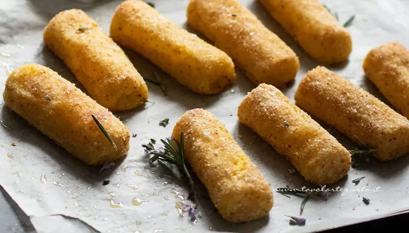 Crocchette di patate al forno dorate e croccanti, pronte per essere gustate. Profumano di rosmarino e sale grosso.