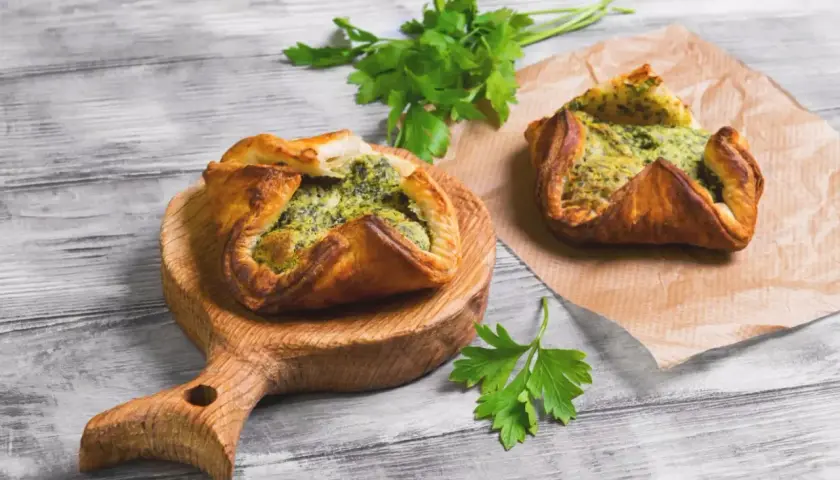 Due fagottini di pasta sfoglia con ripieno verde, uno su tagliere di legno, l'altro su carta forno. Idee su pasta sfoglia cosa mettere dentro.