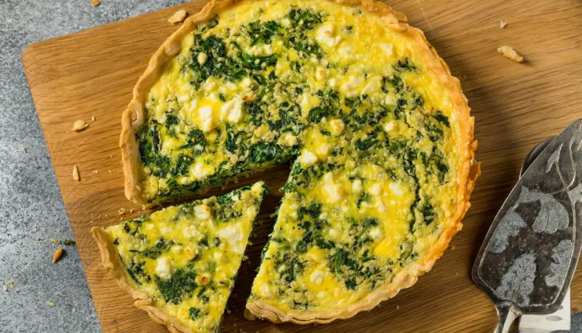 Torta salata ricotta e spinaci dorata e invitante, con una fetta tagliata su un tagliere di legno.