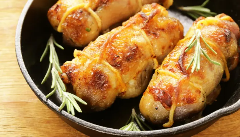 Involtini di pollo dorati e succulenti, legati con spago da cucina e guarniti con rametti di rosmarino, serviti in una padella di ghisa.