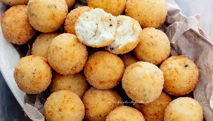 Un cesto pieno di croccanti polpette di ricotta, dorate e invitanti. Una è aperta, mostrando il morbido interno.