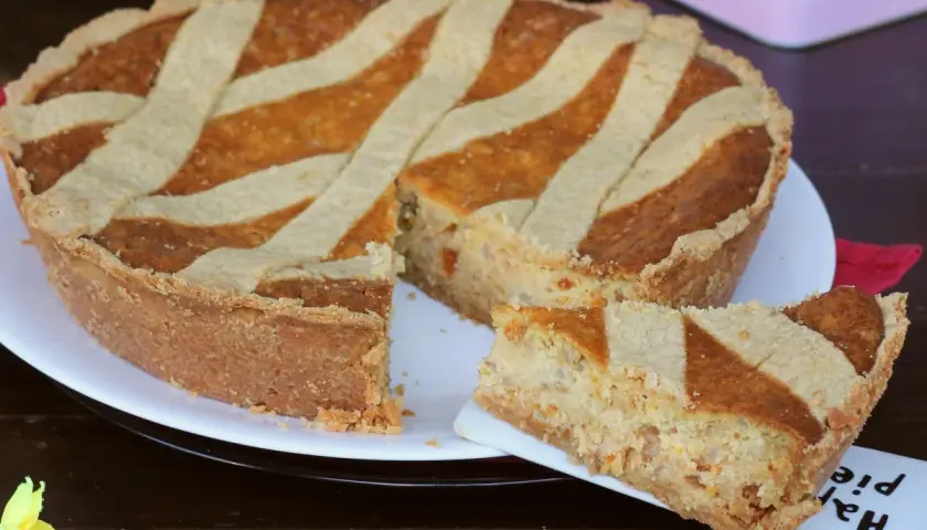 Una pastiera giallo zafferano, con una fetta servita su un piattino, pronta per essere gustata.