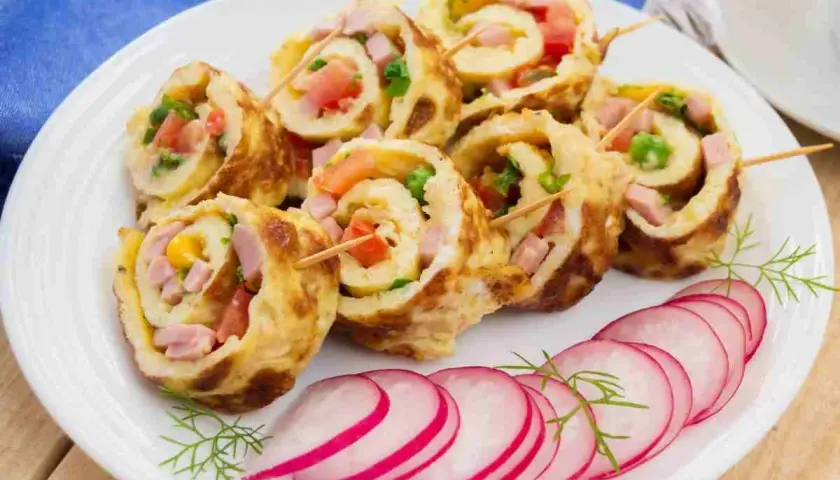 Rotolo di frittata ripieno di prosciutto, pomodoro e verdure, servito con fettine di ravanello.