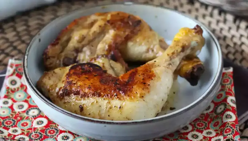 Cosce di pollo in padella, dorate e succulente, servite in una ciotola su un tovagliolo decorato.