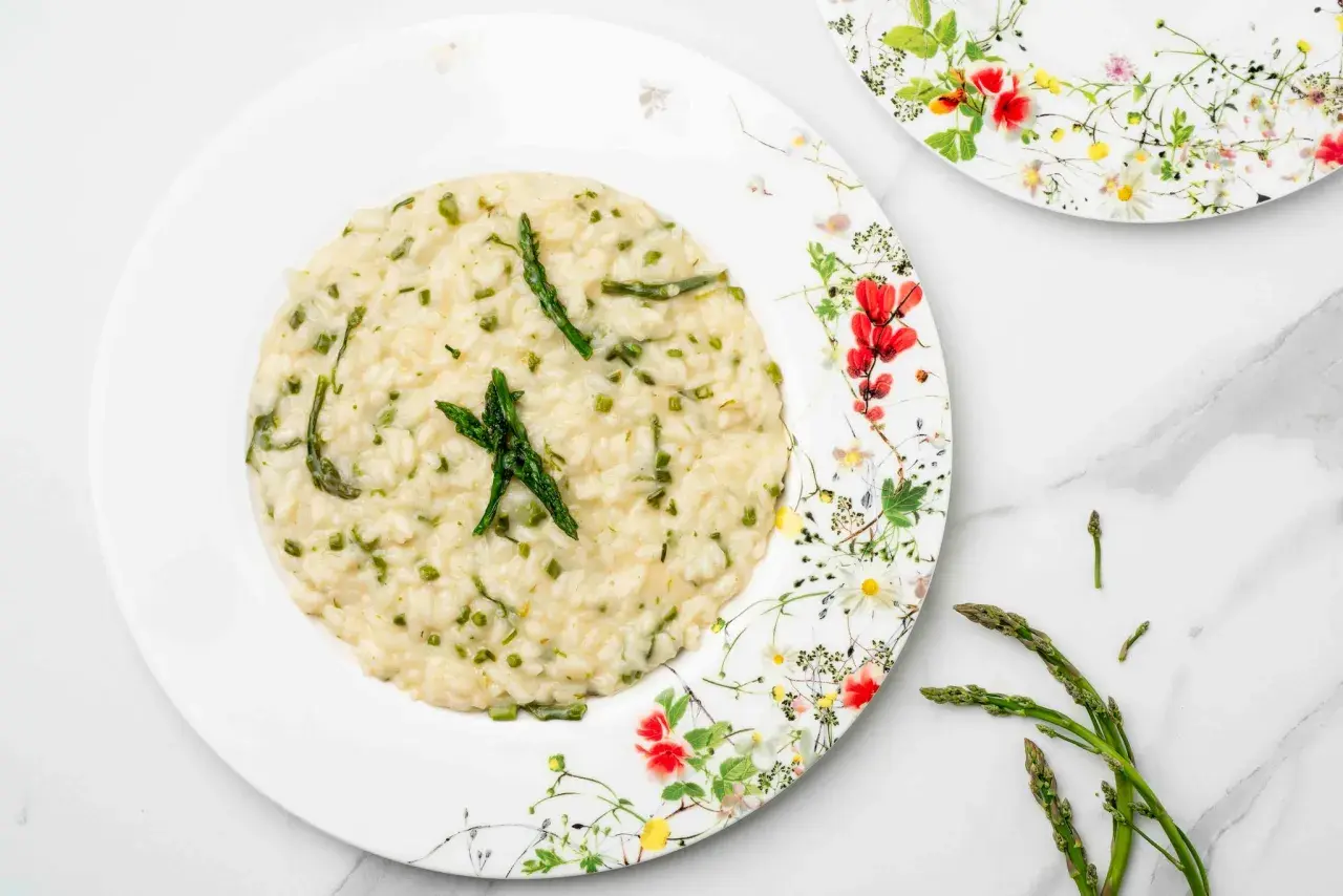 Un cremoso risotto con asparagi selvatici, guarnito con punte di asparago fresco su un piatto fiorito.