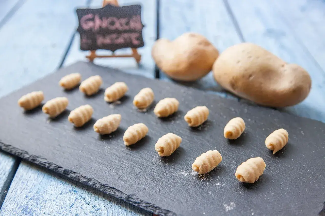 Gnocchi fatti in casa, morbidi e rigati, pronti per essere cucinati. Due patate sullo sfondo, ingredienti freschi per un piatto delizioso.