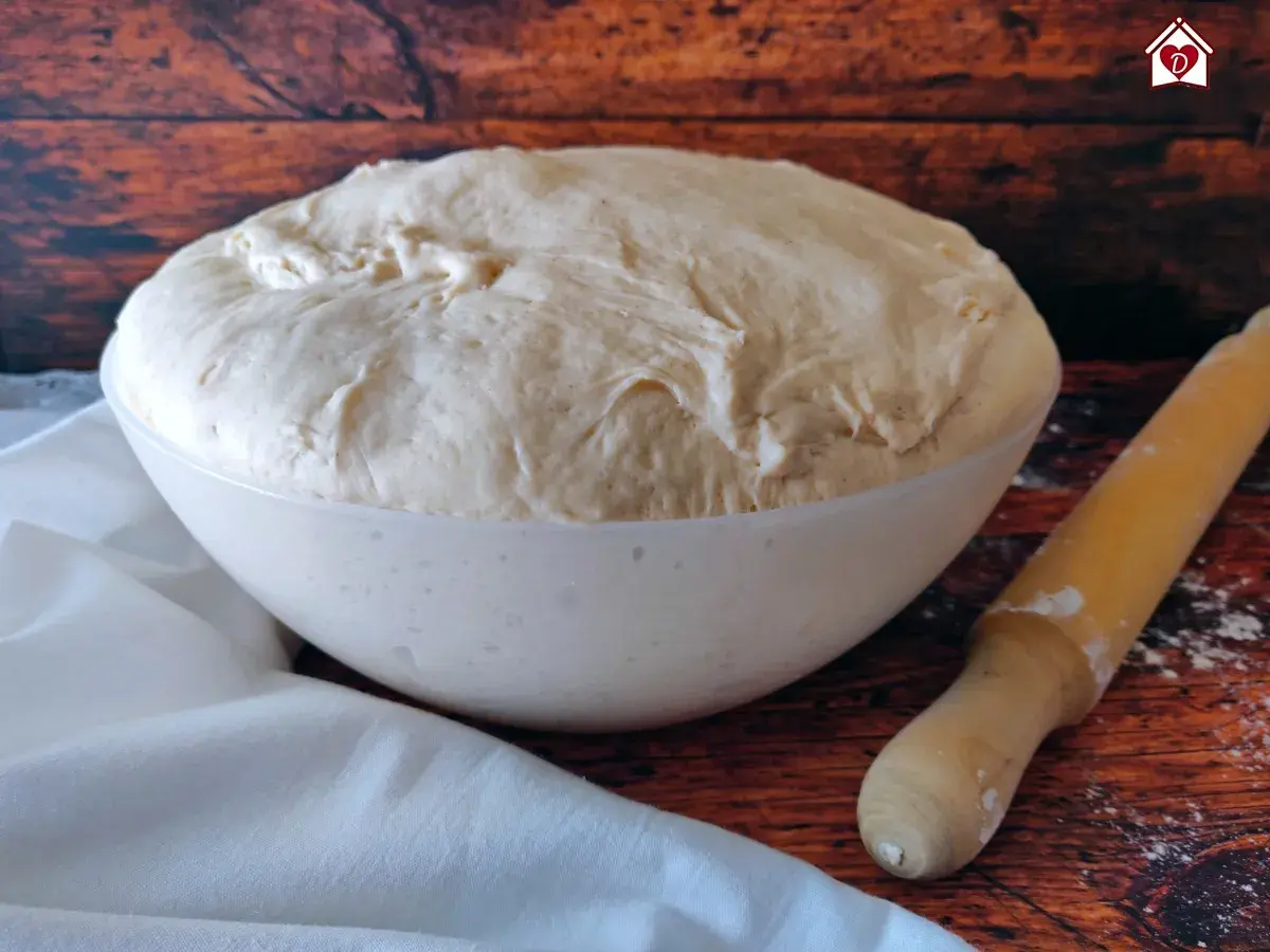 Impasto lievitato per pizza fatta in casa in una ciotola, pronto per essere steso con il mattarello.