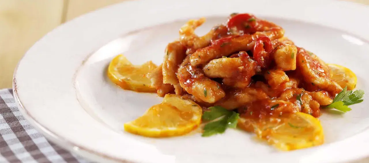 Straccetti di pollo al limone succulenti, conditi con salsa rossa e guarniti con fette di limone e prezzemolo fresco.