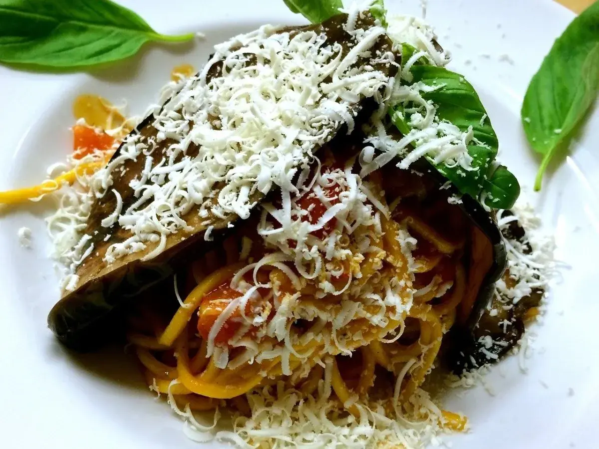 Pasta alla Norma ricetta: spaghetti con melanzane fritte, pomodoro e ricotta salata grattugiata, guarnita con basilico fresco.