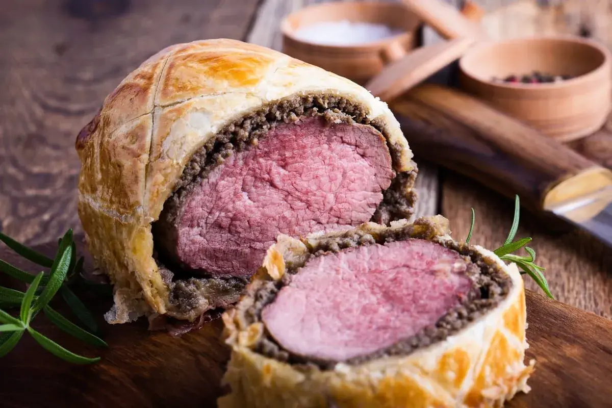 Un succulento filetto alla Wellington, tagliato a metà, rivela la sua carne rosa e tenera, avvolta in pasta sfoglia dorata e funghi.