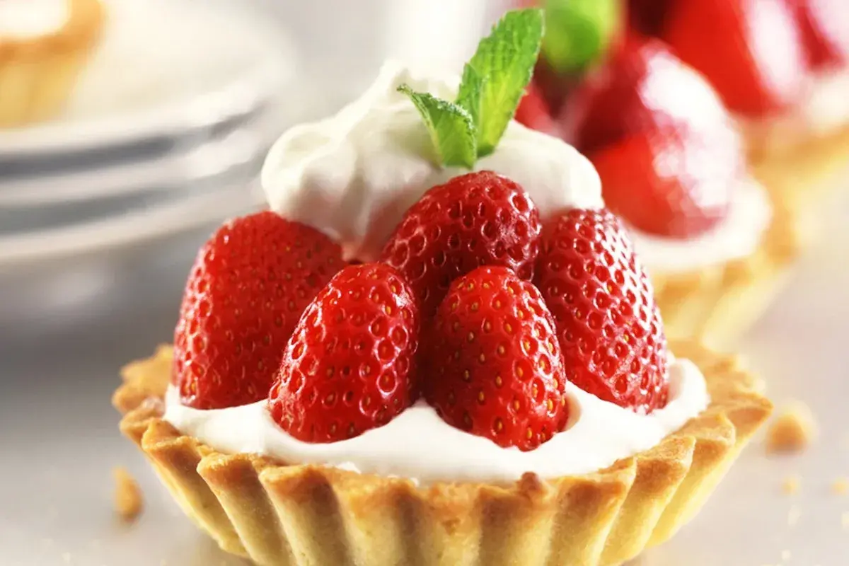 Deliziosi dolci con fragole fresche e panna montata, guarniti con una fogliolina di menta.