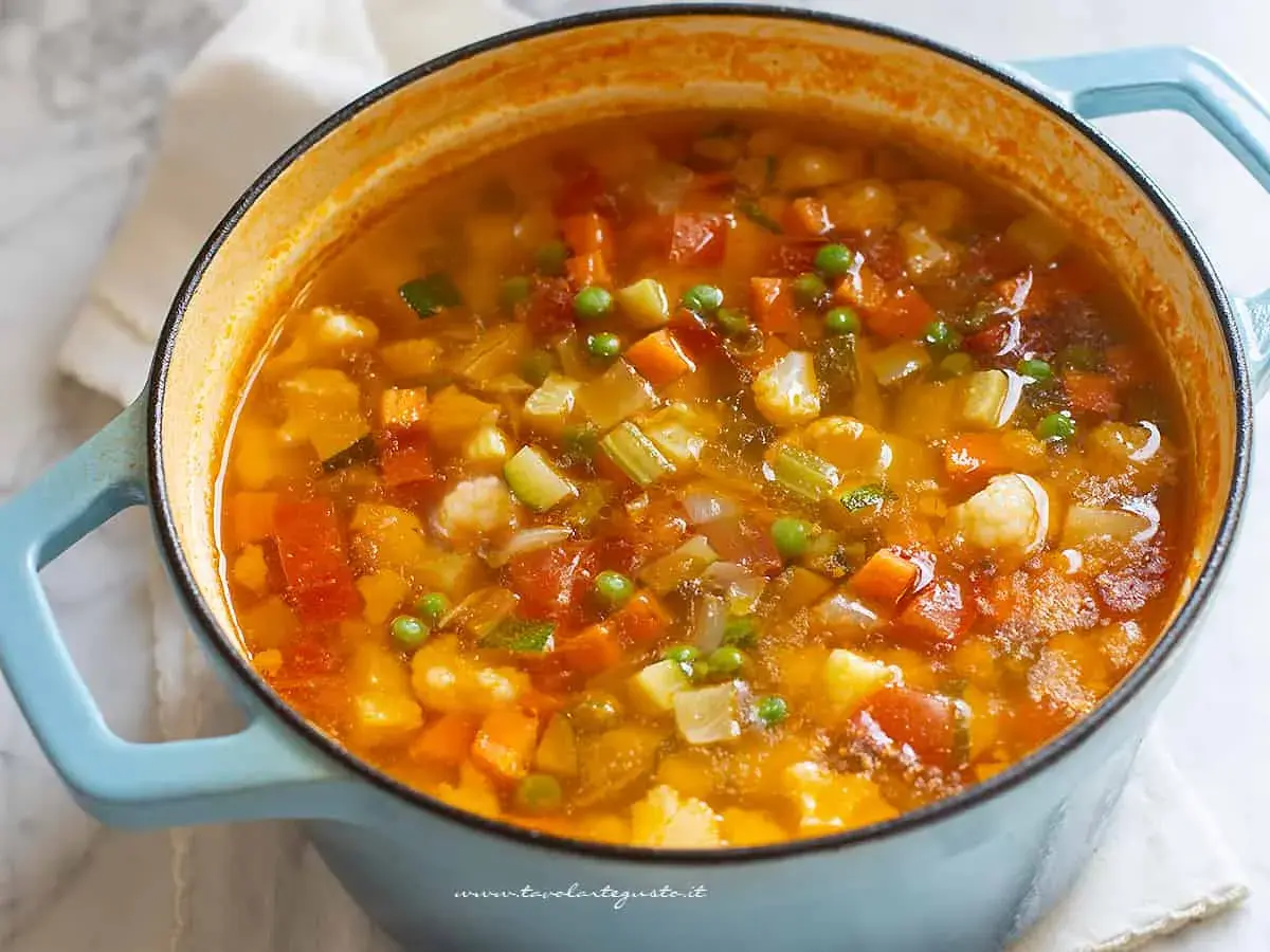 A close-up of a light blue pot filled with steaming minestrone soup, showing chunks of vegetables.