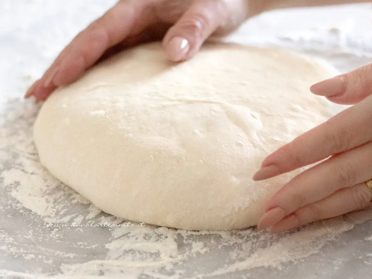 Mani che lavorano un impasto soffice, pronto per diventare una pizza giallo zafferano.