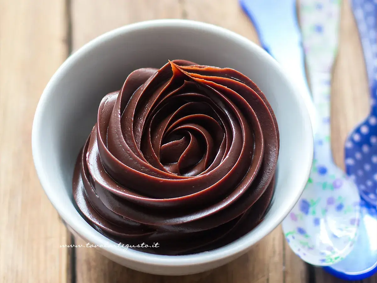 Una ciotola bianca piena di ganache al cioccolato, con un vortice perfetto. Vicino, cucchiai colorati.