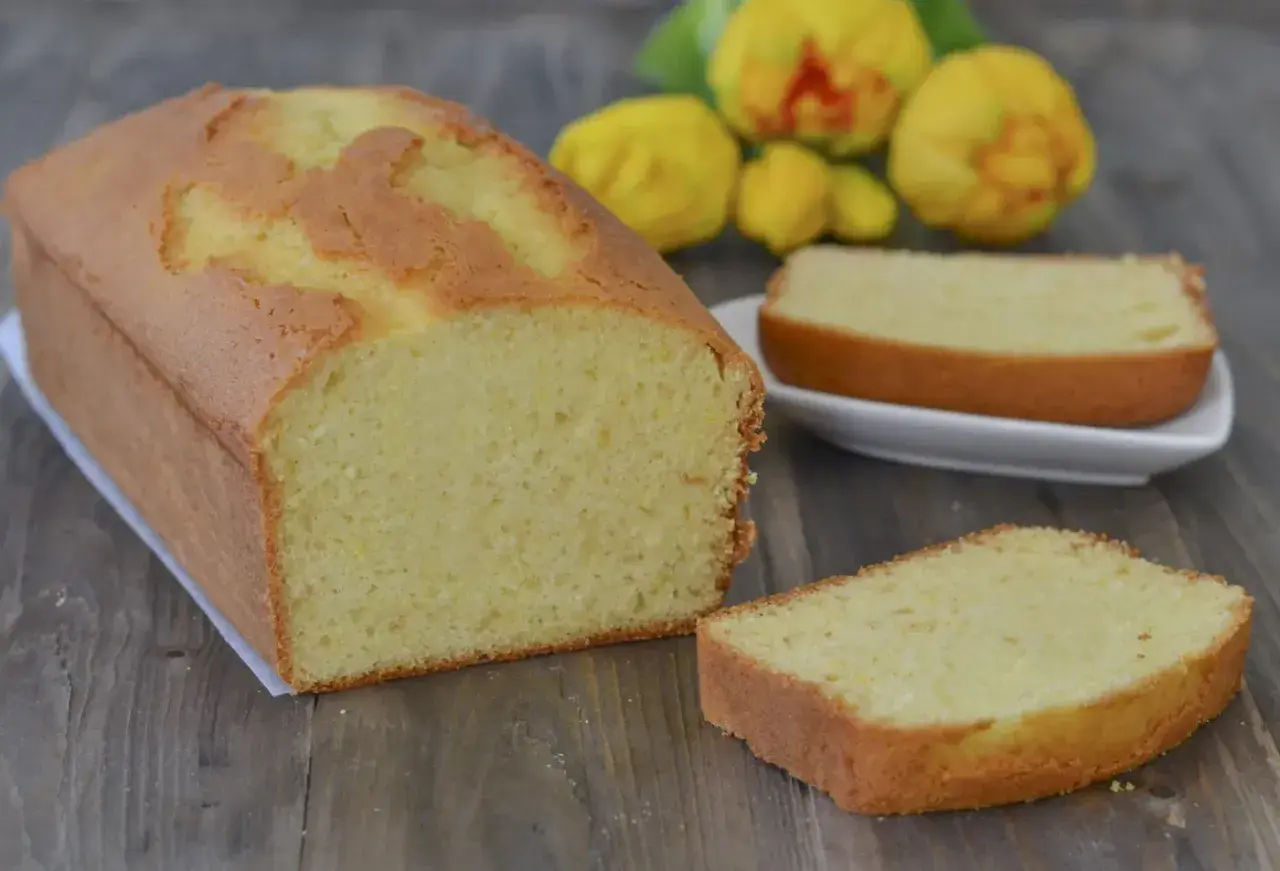 Plumcake al limone soffice e profumato, con una fetta tagliata e pronta da gustare. Sullo sfondo, limoni freschi.