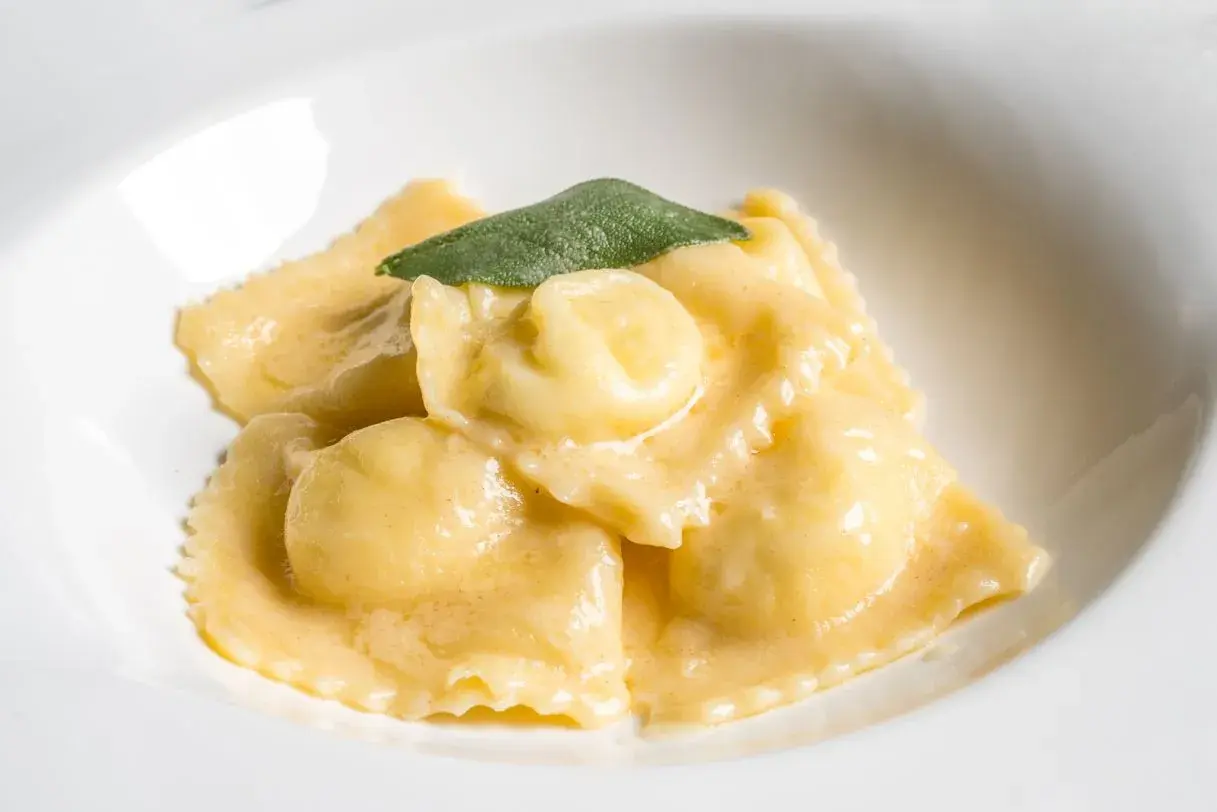 Ravioli dorati in salsa cremosa, guarniti con una foglia di salvia. Il ripieno per ravioli è un segreto gustoso.
