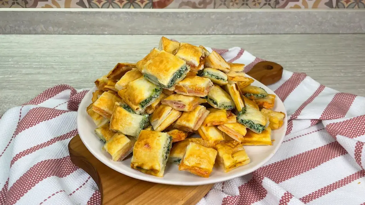 Un mucchio di salatini con pasta sfoglia, alcuni ripieni di spinaci e altri di prosciutto, pronti per essere gustati.