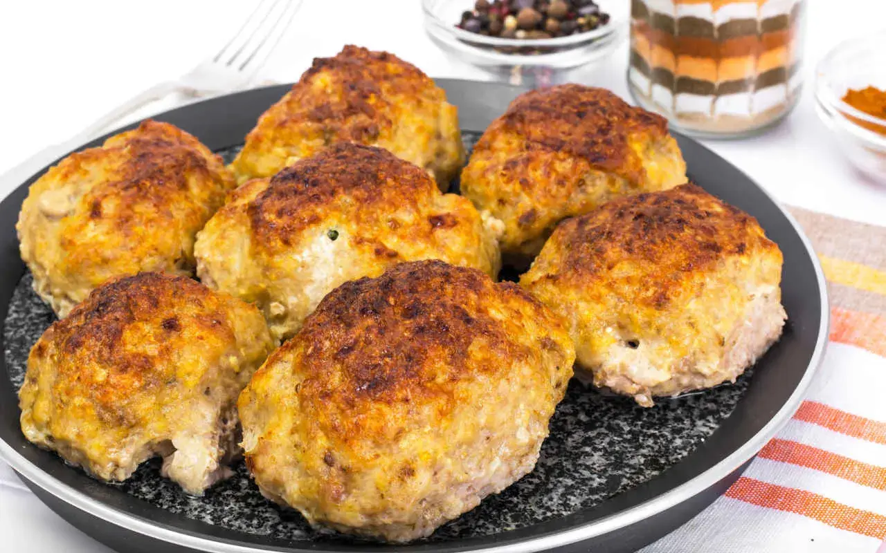 Golden brown zucchini and potato fritters on a black pan.