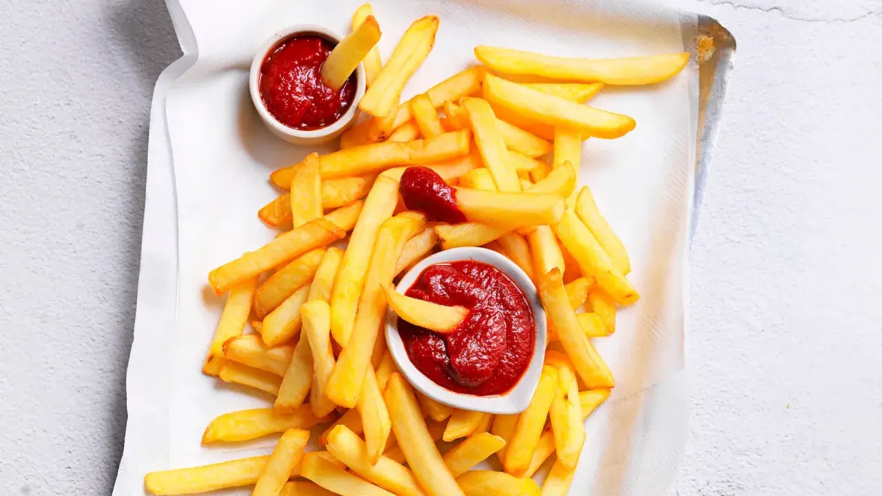 Patatine fritte dorate e croccanti con due ciotoline di ketchup fatto in casa, una con una patatina che si tuffa dentro.