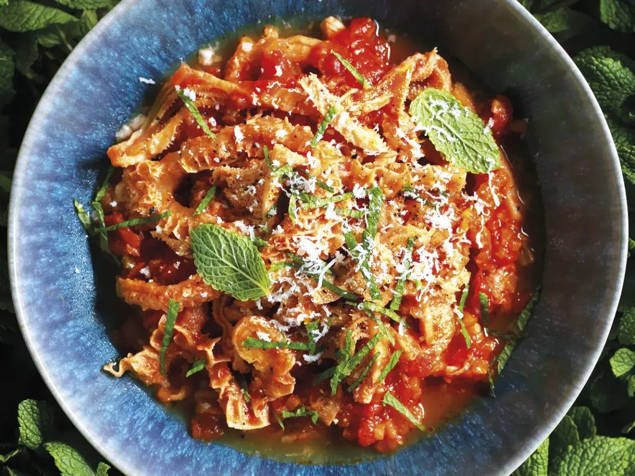 Un piatto fumante di trippa alla romana, condita con pomodoro, pecorino e menta fresca, servita in una ciotola blu.
