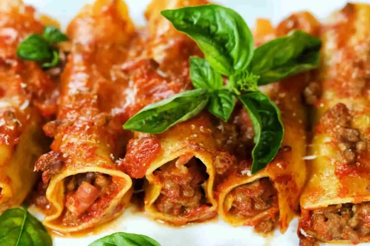 Cannelloni di carne ricetta della nonna, ripieni di ragù e conditi con sugo rosso e basilico fresco.