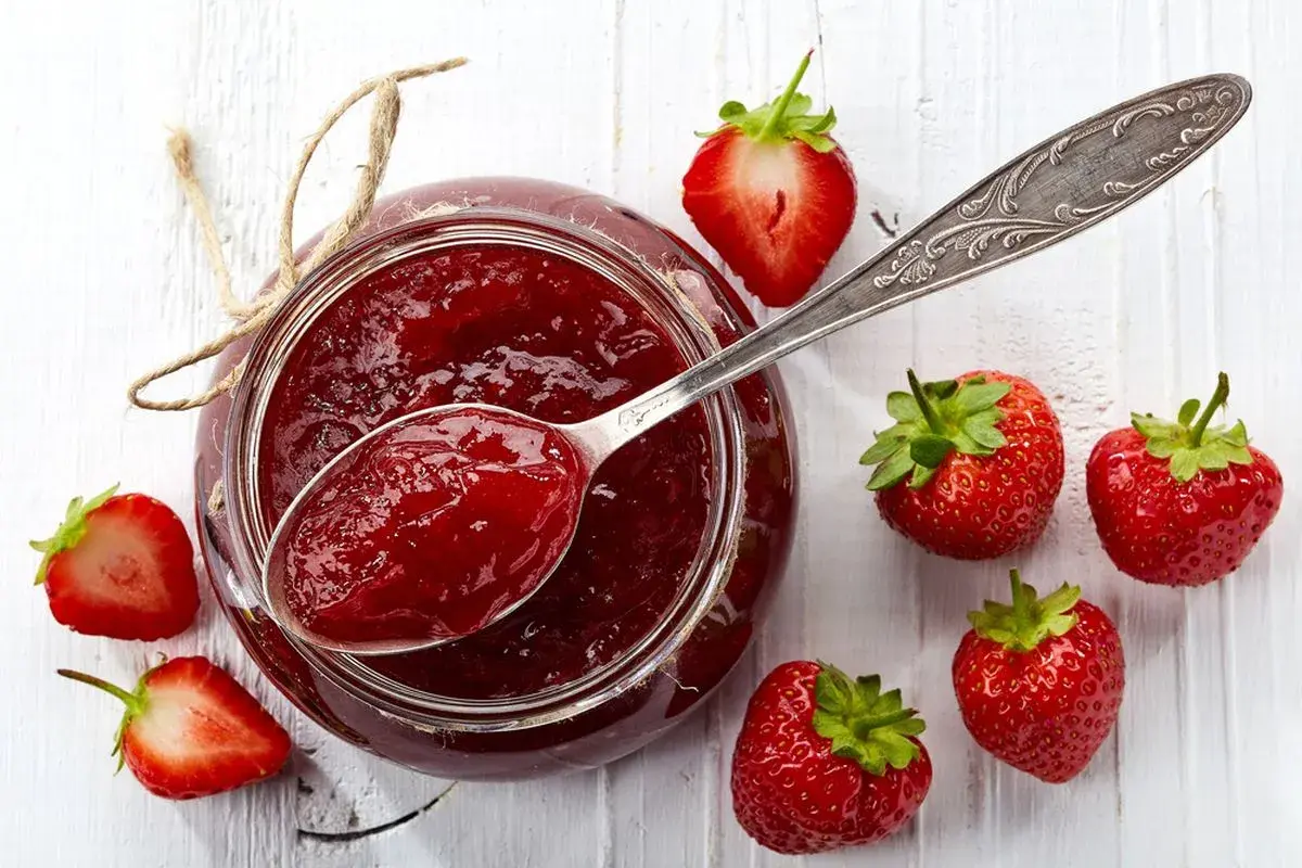 Un vasetto di marmellata di fragole fatto in casa, con fragole fresche e un cucchiaio pieno di dolcezza rossa.