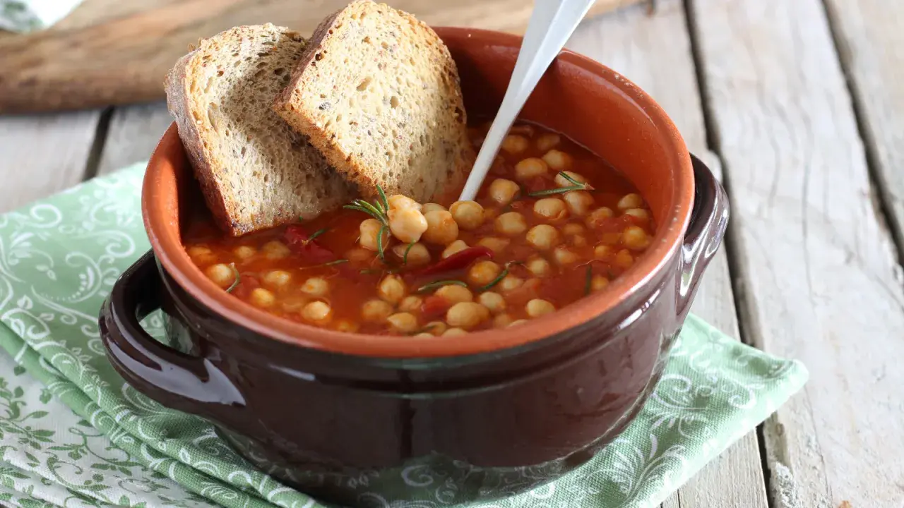 Una ciotola di terracotta con zuppa di ceci, pomodoro e rosmarino, accompagnata da fette di pane rustico.