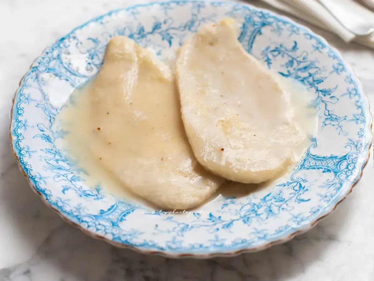 Due scaloppine al vino bianco, tenere e succulente, servite su un piatto di ceramica decorato con motivi blu.