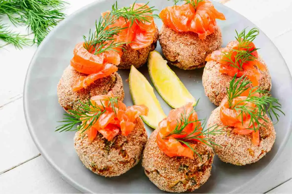 Polpette di pesce dorate, guarnite con salmone affumicato, aneto e spicchi di lime. Un antipasto raffinato e gustoso.