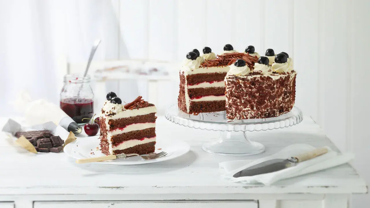 Una fetta di foresta nera torta, con strati di cioccolato, panna e ciliegie, accanto a una torta intera decorata.