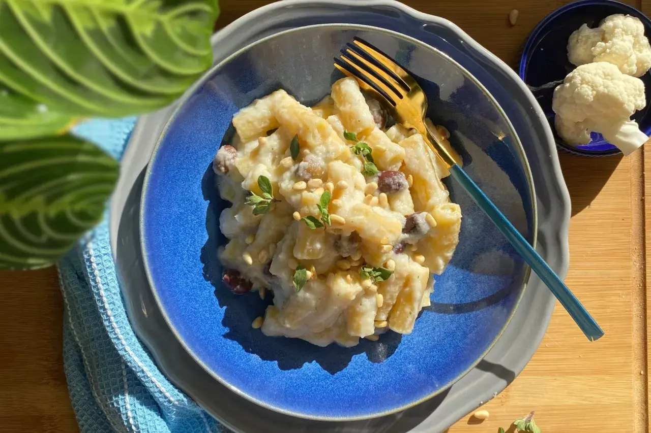 Piatto di pasta e cavolfiore cremoso, guarnito con pinoli e erbe aromatiche, pronto per essere gustato.