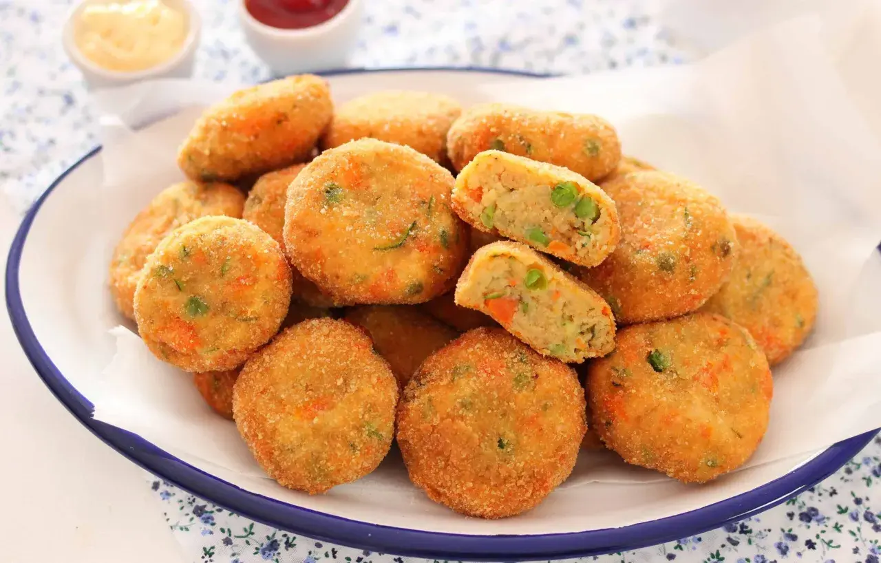 Un piatto pieno di polpette di verdure al forno, dorate e croccanti, con piselli e carote visibili all'interno.