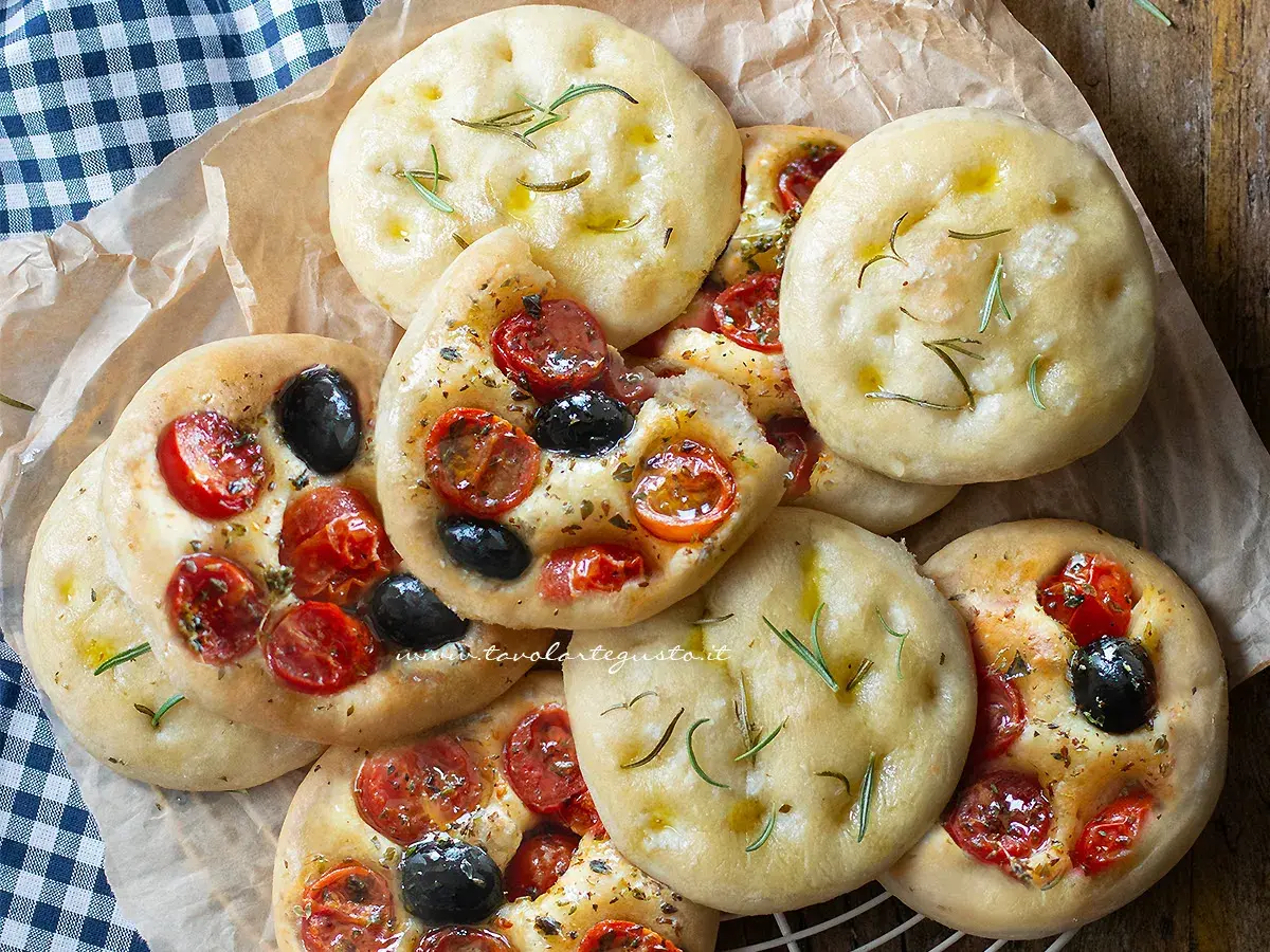 Focaccine in padella, alcune condite con pomodorini e olive, altre con rosmarino e olio. Perfette per uno spuntino.