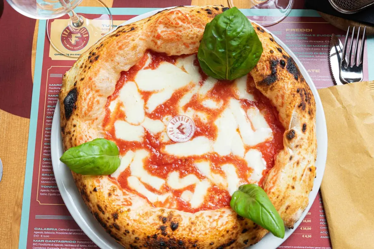Impasto pizza napoletana con pomodoro, mozzarella filante e basilico fresco. La crosta è alta e alveolata, segno di una lievitazione perfetta.