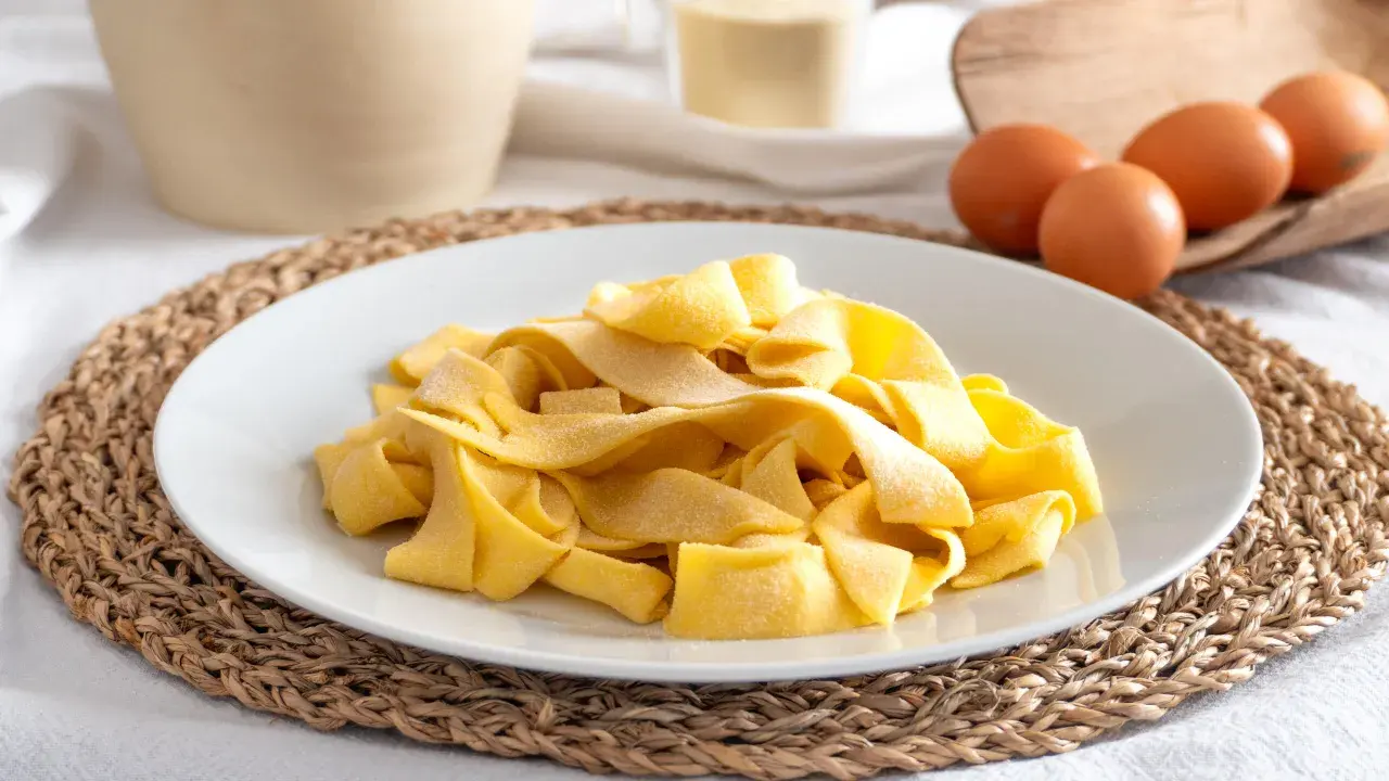 Piatto di pasta fresca fatta in casa, con uova e farina sullo sfondo.
